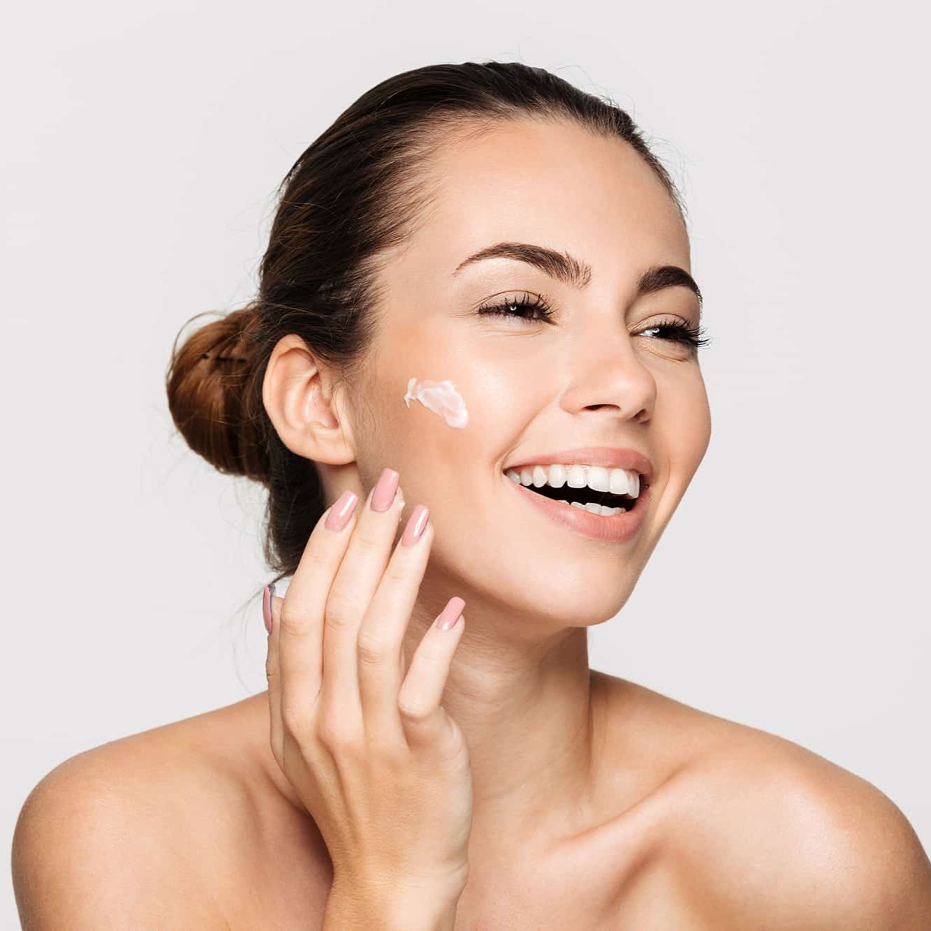Mujer sonriendo mientras se aplica crema facial en una rutina de cuidado de la piel
